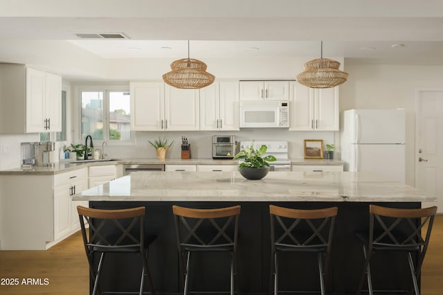 kitchen with pendant lighting, white appliances, a kitchen bar, and a center island