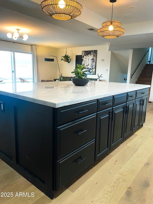 kitchen featuring light stone counters, hanging light fixtures, and light hardwood / wood-style floors