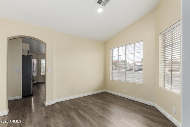 unfurnished room featuring lofted ceiling, baseboards, arched walkways, dark wood-style floors, and visible vents