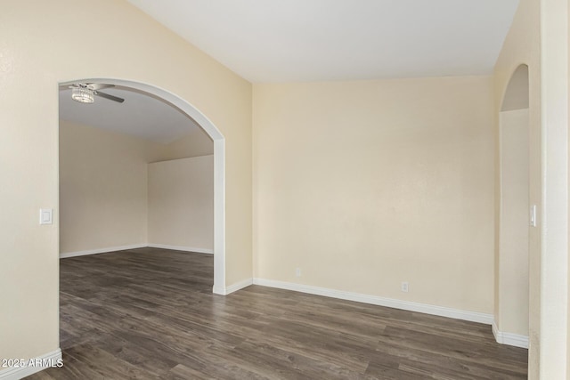 empty room featuring dark wood-style floors, arched walkways, baseboards, and a ceiling fan
