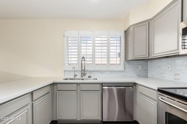 kitchen featuring gray cabinets, light countertops, a sink, tasteful backsplash, and appliances with stainless steel finishes