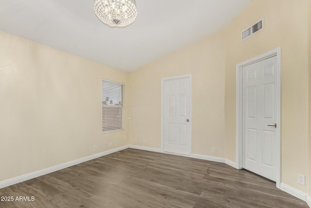 empty room with lofted ceiling, dark wood-style flooring, visible vents, and an inviting chandelier