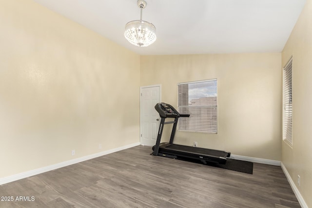 workout area featuring baseboards, wood finished floors, vaulted ceiling, and a notable chandelier