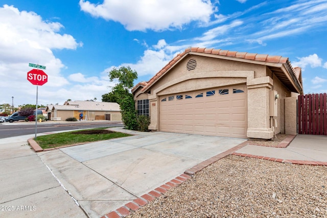 exterior space featuring a tile roof, concrete driveway, stucco siding, fence, and a garage