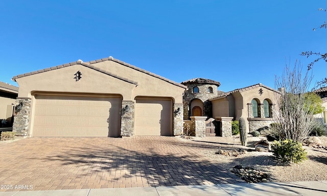 mediterranean / spanish house featuring an attached garage, stone siding, a tiled roof, decorative driveway, and stucco siding