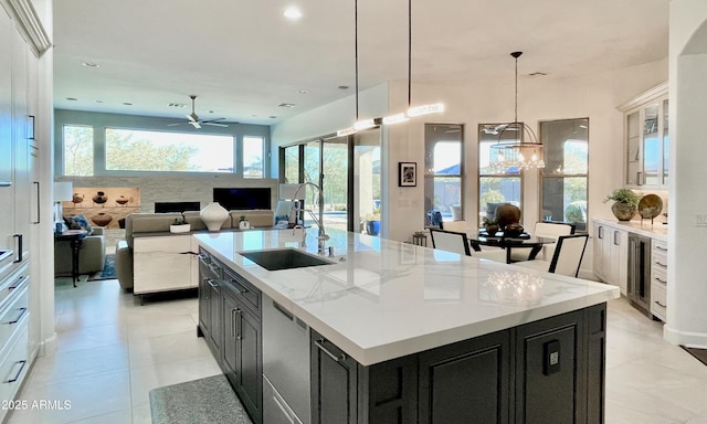 kitchen with a kitchen island with sink, white cabinetry, a sink, light stone countertops, and dishwasher