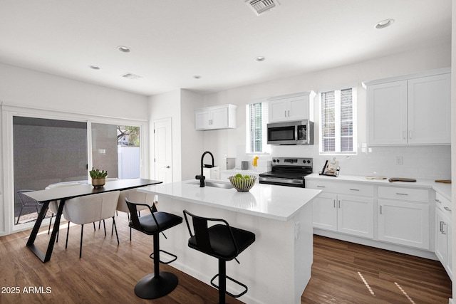 kitchen with stainless steel appliances, a sink, backsplash, an island with sink, and white cabinetry