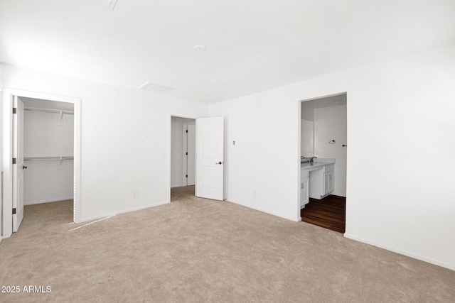 unfurnished bedroom featuring light colored carpet, a walk in closet, baseboards, and ensuite bathroom