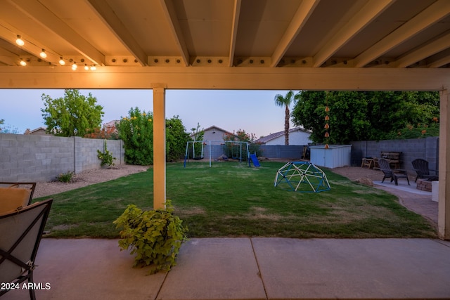 yard at dusk with a patio, a playground, and a storage shed