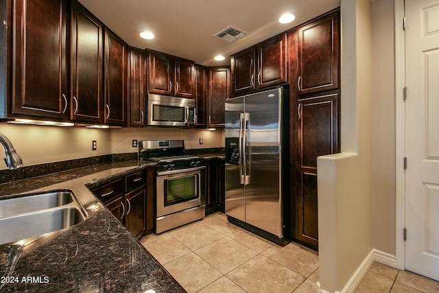 kitchen with dark stone counters, sink, appliances with stainless steel finishes, dark brown cabinets, and light tile patterned flooring