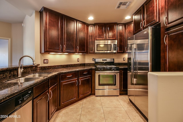 kitchen featuring light tile patterned flooring, sink, stainless steel appliances, and dark stone counters