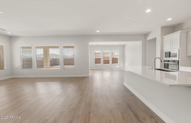 22660 E Pegasus Pkwy, Queen Creek, AZ 85142 - unfurnished living room with recessed lighting, light wood finished floors, a sink, and baseboards