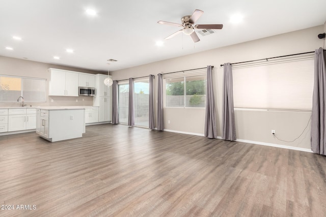 kitchen with a kitchen island, sink, pendant lighting, light wood-type flooring, and white cabinetry