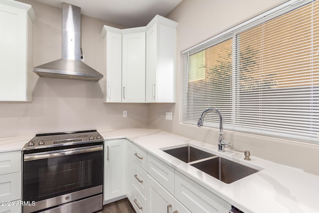 kitchen with wall chimney range hood, white cabinetry, stainless steel range with electric cooktop, and sink