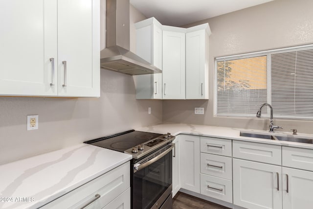 kitchen with electric range, light stone counters, white cabinetry, wall chimney exhaust hood, and sink