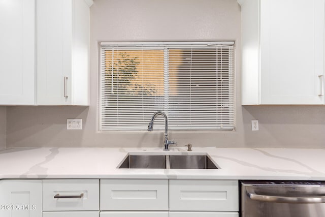 kitchen with stainless steel dishwasher, sink, white cabinets, and light stone countertops