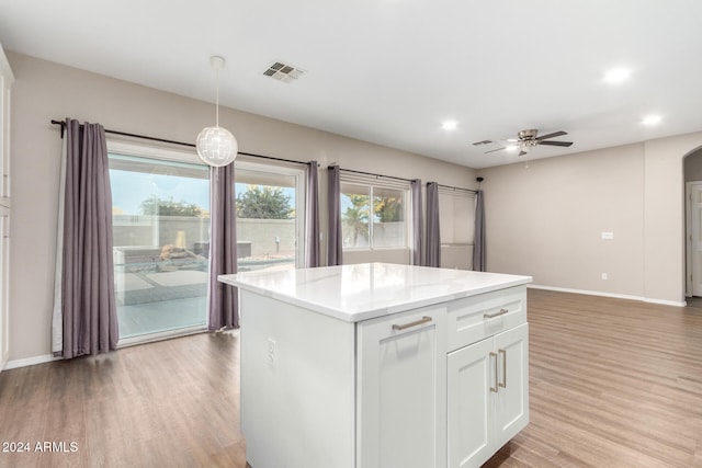 kitchen with a kitchen island, white cabinetry, light hardwood / wood-style floors, pendant lighting, and light stone counters