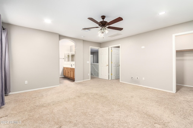 unfurnished bedroom featuring a walk in closet, ensuite bath, light colored carpet, and ceiling fan