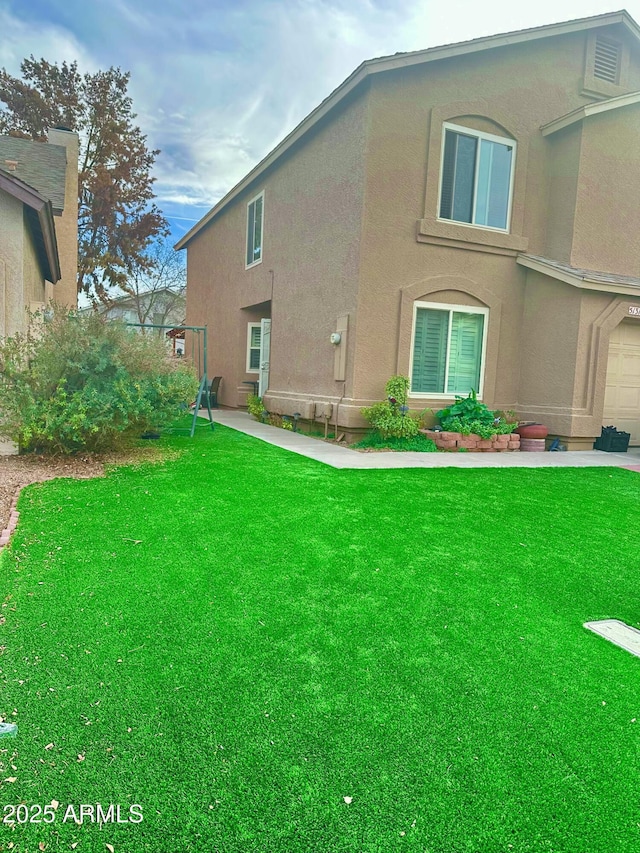 back of property with a garage, a yard, and stucco siding