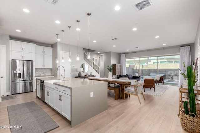 kitchen featuring stainless steel refrigerator with ice dispenser, decorative light fixtures, light hardwood / wood-style flooring, a kitchen island with sink, and white cabinets