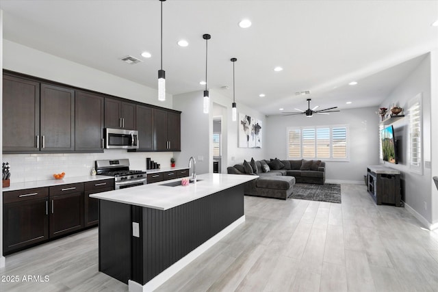 kitchen featuring a center island with sink, stainless steel appliances, sink, decorative backsplash, and pendant lighting