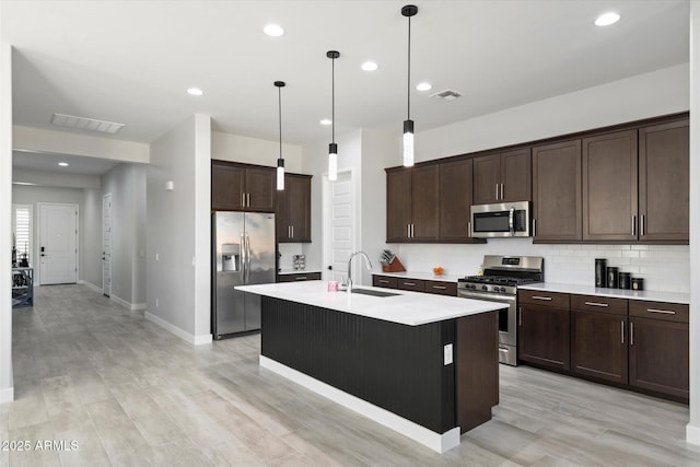 kitchen with stainless steel appliances, pendant lighting, backsplash, sink, and a kitchen island with sink