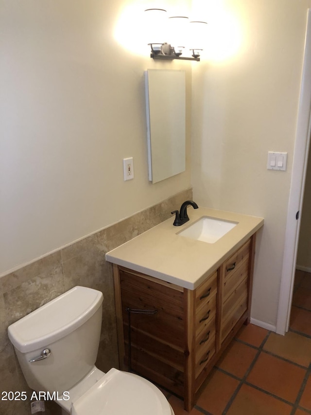 bathroom with toilet, tile walls, vanity, wainscoting, and tile patterned floors