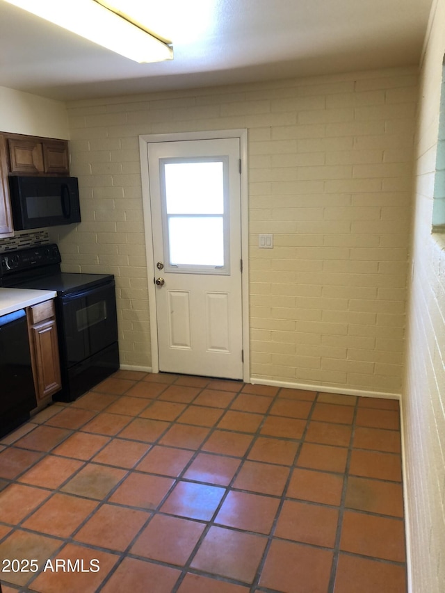 kitchen with light tile patterned floors, black appliances, and brick wall