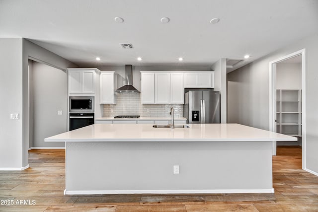 kitchen with visible vents, a sink, a spacious island, appliances with stainless steel finishes, and wall chimney exhaust hood