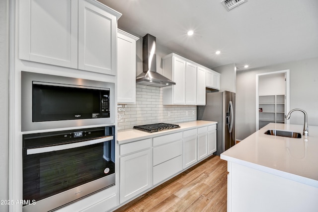 kitchen with wall chimney range hood, white cabinets, appliances with stainless steel finishes, and a sink