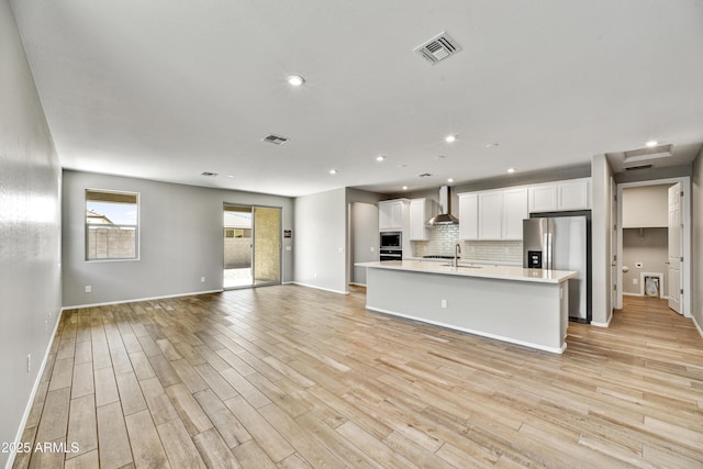 kitchen with tasteful backsplash, open floor plan, light countertops, appliances with stainless steel finishes, and wall chimney exhaust hood