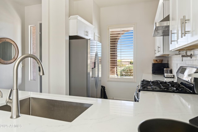 kitchen featuring tasteful backsplash, under cabinet range hood, stainless steel appliances, white cabinetry, and a sink