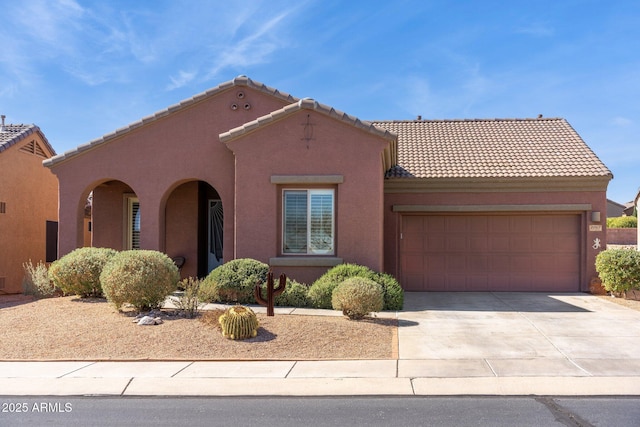 mediterranean / spanish home with stucco siding, a tiled roof, concrete driveway, and a garage