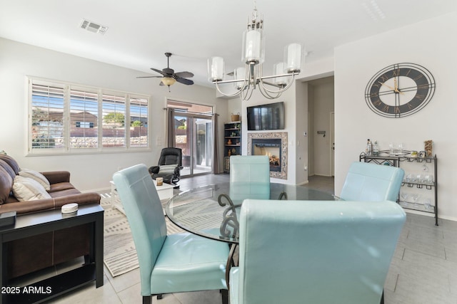 dining area featuring baseboards, visible vents, a lit fireplace, tile patterned flooring, and ceiling fan with notable chandelier