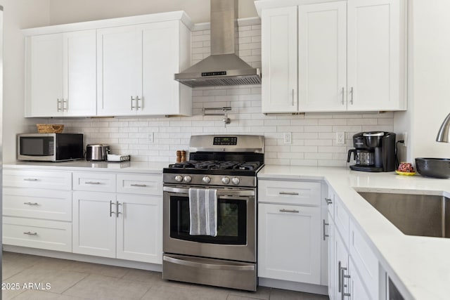 kitchen with backsplash, wall chimney range hood, stainless steel appliances, white cabinetry, and a sink