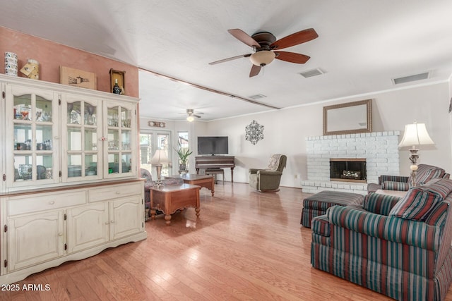 living room with ceiling fan, crown molding, light wood-type flooring, and a brick fireplace