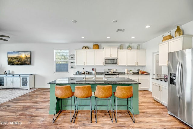 kitchen featuring white cabinetry, appliances with stainless steel finishes, a kitchen bar, and an island with sink