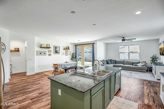 kitchen with sink, green cabinets, wood-type flooring, an island with sink, and stainless steel dishwasher