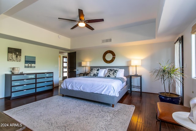 bedroom with dark hardwood / wood-style flooring, a raised ceiling, and ceiling fan