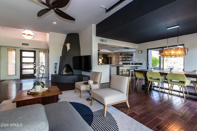 living room featuring dark hardwood / wood-style flooring, ceiling fan with notable chandelier, and a large fireplace