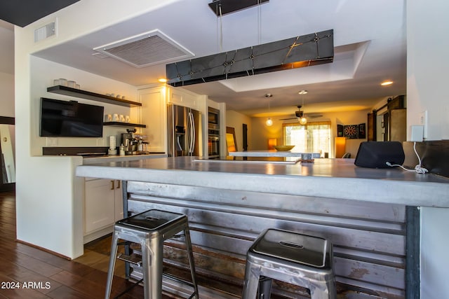 kitchen featuring dark wood-type flooring, a breakfast bar area, ceiling fan, appliances with stainless steel finishes, and white cabinetry