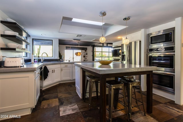 kitchen with pendant lighting, appliances with stainless steel finishes, white cabinetry, a kitchen breakfast bar, and a kitchen island