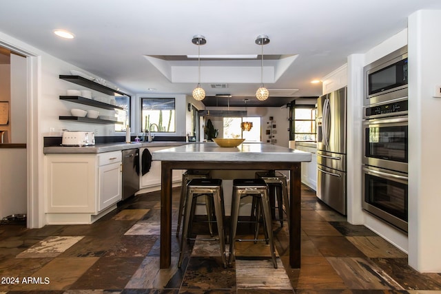 kitchen featuring a kitchen bar, white cabinetry, appliances with stainless steel finishes, a raised ceiling, and pendant lighting