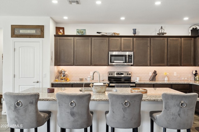 1135 E Barrus Dr, Casa Grande, AZ 85122 - kitchen featuring dark brown cabinets, tasteful backsplash, appliances with stainless steel finishes, a sink, and an island with sink