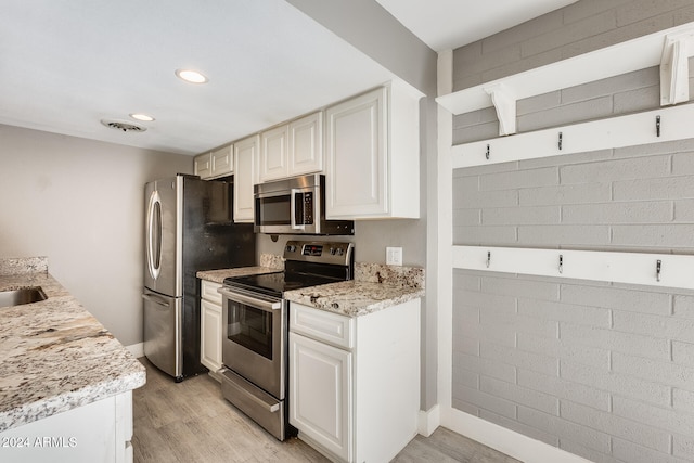 kitchen featuring white cabinetry, light wood-type flooring, stainless steel appliances, sink, and light stone counters