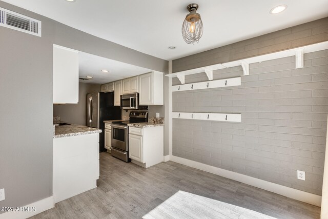 kitchen featuring white cabinets, appliances with stainless steel finishes, light wood-type flooring, decorative light fixtures, and light stone counters