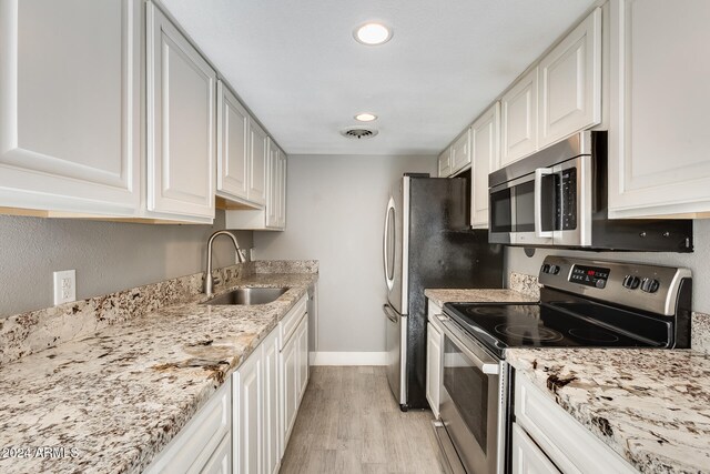 kitchen with stainless steel appliances, sink, light wood-type flooring, white cabinetry, and light stone counters