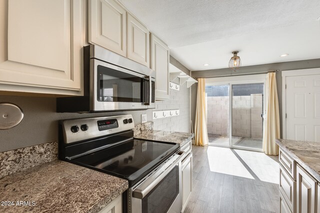 kitchen featuring appliances with stainless steel finishes, light wood-type flooring, a textured ceiling, light stone counters, and decorative backsplash