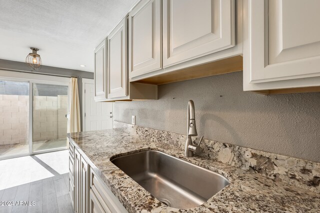 kitchen with sink, a textured ceiling, light hardwood / wood-style floors, white cabinets, and light stone counters