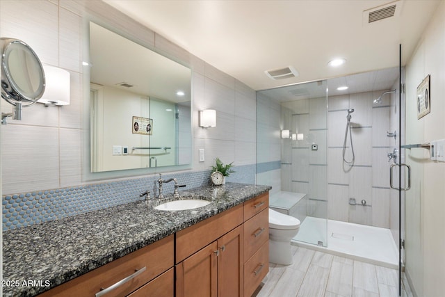 bathroom with toilet, tile walls, a shower with shower door, and vanity